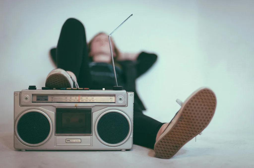 A young woman lying down on the floor with her right foot set atop an old boombox.